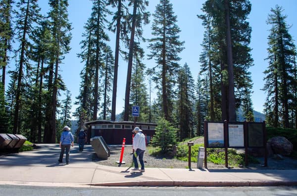 Two people walk along a paved pathway toward a small brown building. - NPS Photo