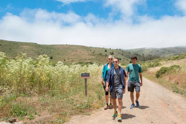 Three hikers walk along the exposed trail to Haypress Campground under cloudy, blue skies. - NPS Photo