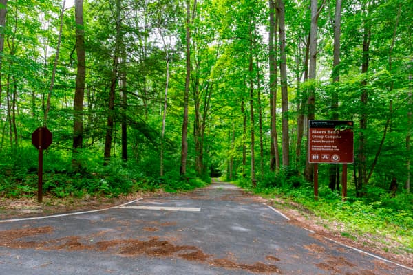 The entrance of Rivers Bend Group Campground shows a driveway into the woods and a sign to the right - NPS Photo / Michael Cuff