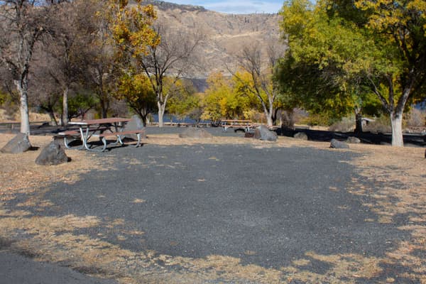 A wide grey gravel parking area is adjacent to a brown and silver picnic bench. - NPS / S. Peterson