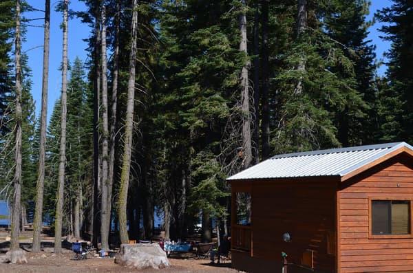 The rear of a wooden cabin in a forest with a partial view of a lake. - NPS Photo