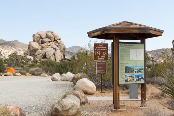 An unpaved road and campground signage is surrounded by vegetation and rock formations. - NPS/Brad Sutton