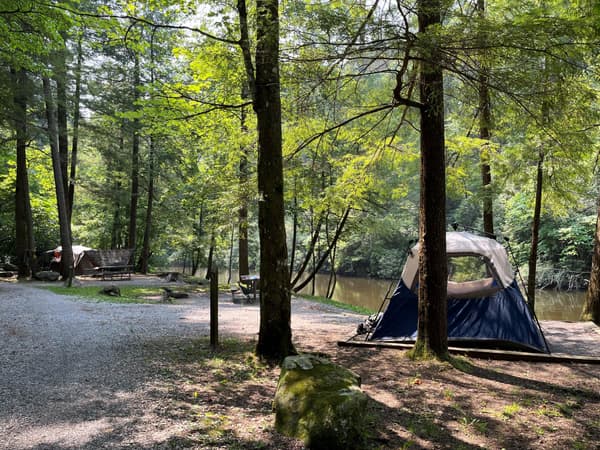 Three campsites in a forested area near a creek, one with a large blue and white tent. - NPS Photo