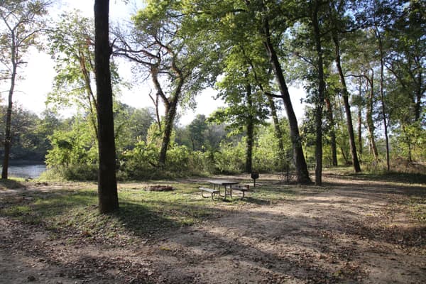 Two campsites with a mix of dirt and grass. Trees provide shade from above. - NPS Photo / Wil Marischen