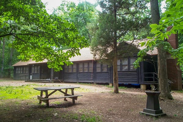A large brown wooden building is surrounded by tree. A picnic table sits on the lawn in front of it - NPS Photo