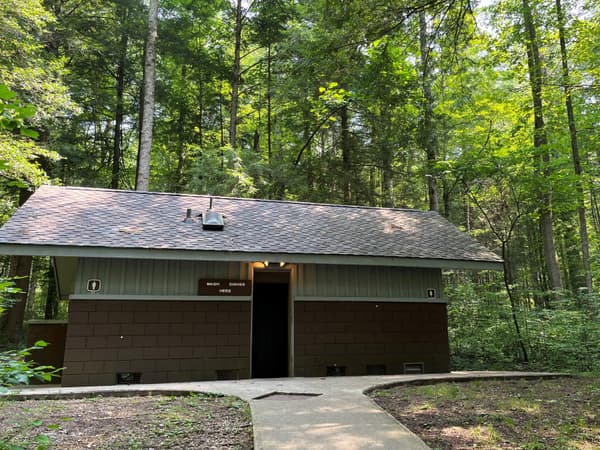 A campground restroom with a paved pathway to it. A sign beside a door says, "Wash dishes here". - NPS Photo