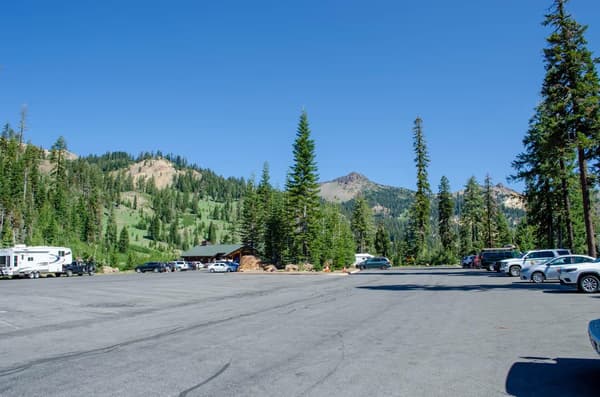 A parking area with vehicles parked on the edges and a building at the far end. - NPS Photo