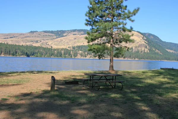picnic table and fire pit next to campsite number post, with lake in background - NPS Photo