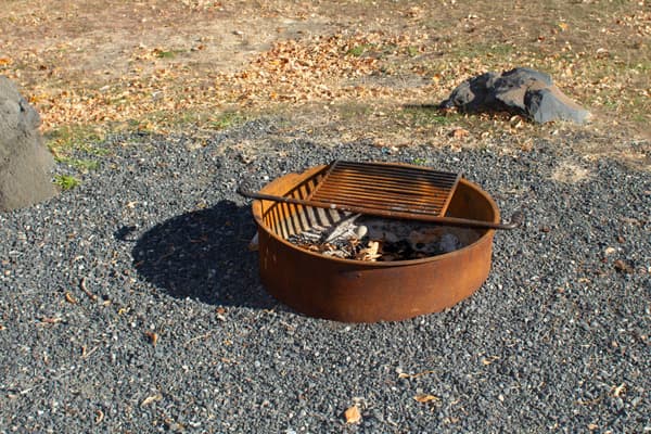 Round rusted metal ring on the ground with a slated grate over the top used for grilling and fires. - NPS / S. Peterson
