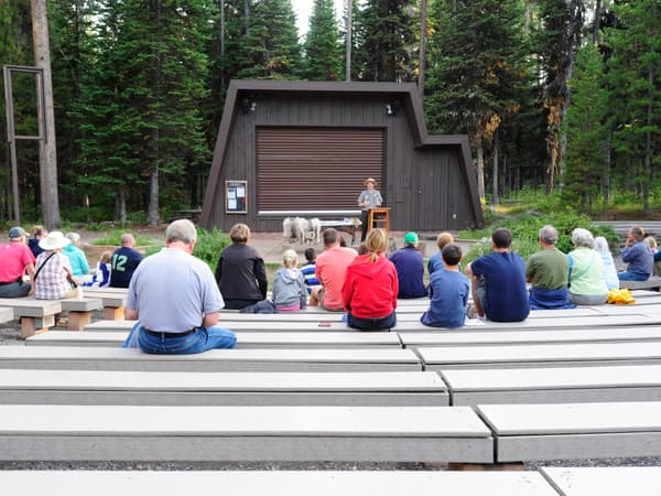 outside amphitheater with visitors sitting on benches and a ranger on stage making a presentation - NPS Photo / Petersen