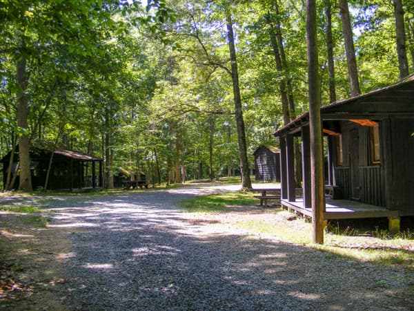Several wooden sleeper cabins are dispersed in the woods with a gravel road between them - NPS Photo