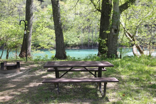 A picnic table and fire ring sit empty, with a blue river in the background. - NPS Photo / Wil Marischen