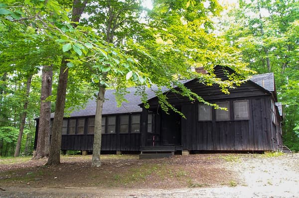 A  dark brown wooden building with a small front porch is among green trees - NPS Photo